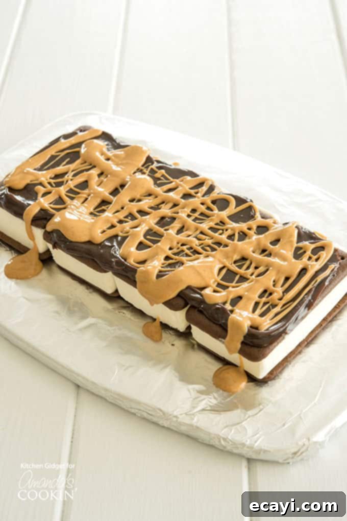 Drizzling Hot Fudge and Peanut Butter on Ice Cream Sandwich Layers A photo illustrating the second step of making the ice cream sandwich cake, showing hot fudge sauce and melted peanut butter drizzled over the first layer of ice cream sandwiches.