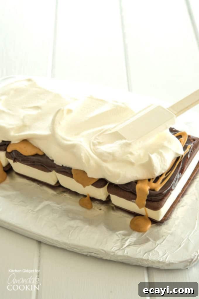Spreading Whipped Topping on Ice Cream Sandwich Cake A photo showing whipped topping being carefully spread over the first ice cream sandwich layer, fudge, and peanut butter.