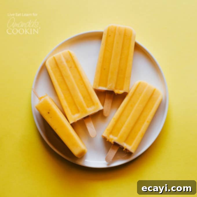 Learn how to make delicious homemade creamsicle popsicles at home! A much healthier option that the creamsicles you buy at the store! With ingredients like orange juice, chopped mango, banana and Greek yogurt, how can you go wrong? #healthydessert #popsicles #homemadepopsicles #healthy #forkids #easy #fruit #popsiclesforkids #homemadepopsiclesforkids #easyhomemadepopsicles #fruitpopsicles #popsiclerecipes #mango #banana #greekyogurt #yogurt #orange #orangejuice #creamsicle Creamsicle Popsicles on a plate, showcasing their vibrant orange color and creamy texture.