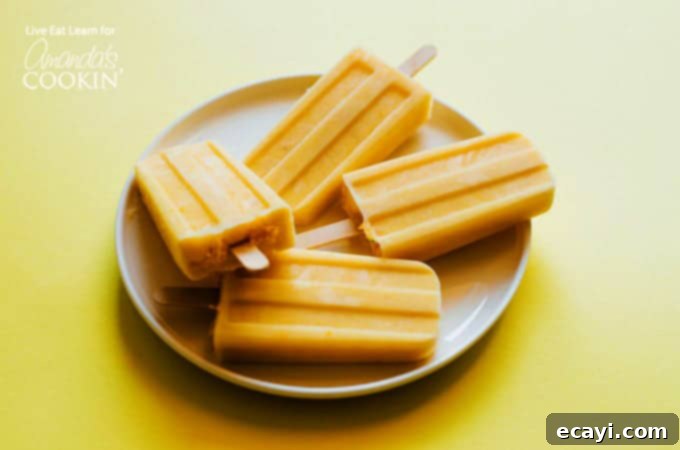 Learn how to make delicious homemade creamsicle popsicles at home! A much healthier option that the creamsicles you buy at the store! With ingredients like orange juice, chopped mango, banana and Greek yogurt, how can you go wrong? #healthydessert #popsicles #homemadepopsicles #healthy #forkids #easy #fruit #popsiclesforkids #homemadepopsiclesforkids #easyhomemadepopsicles #fruitpopsicles #popsiclerecipes #mango #banana #greekyogurt #yogurt #orange #orangejuice #creamsicle A single Tropical Orange Creamsicle Popsicle shown on a plate, highlighting its smooth texture and refreshing appeal.