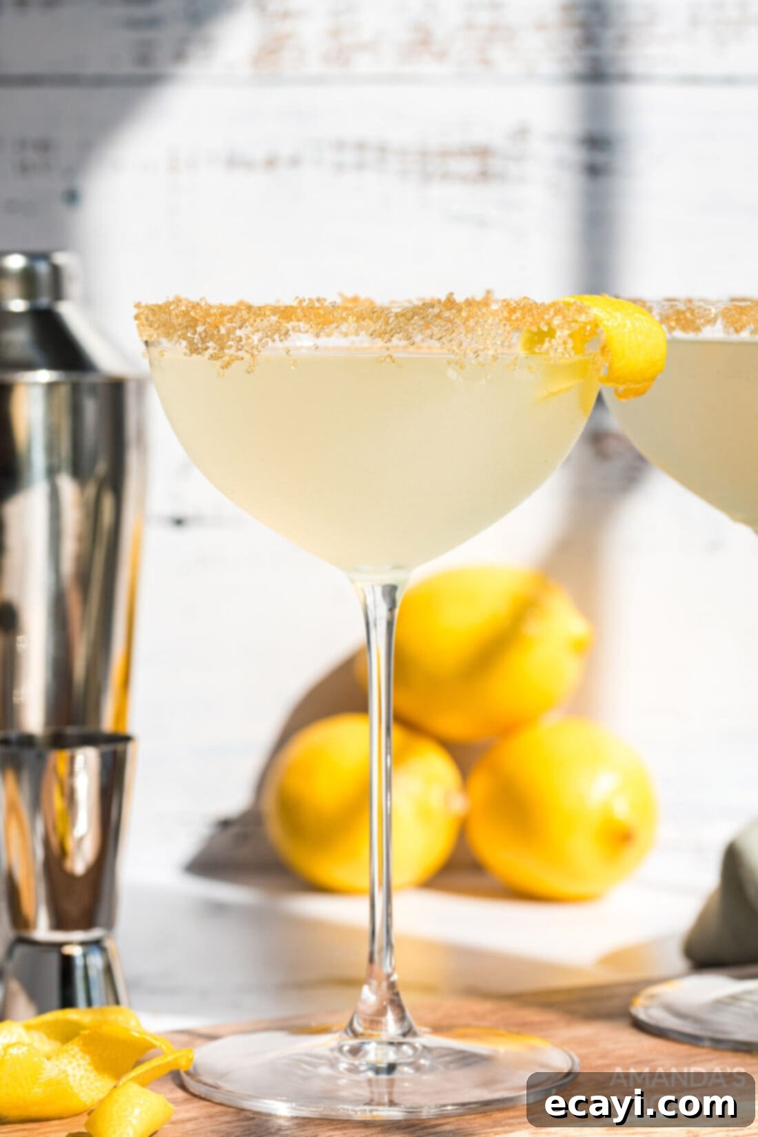 Sweet Tart Twinkle 10 Beautifully garnished Lemon Drop Cocktail with a sugared rim and a curly lemon twist, set against a warm background.