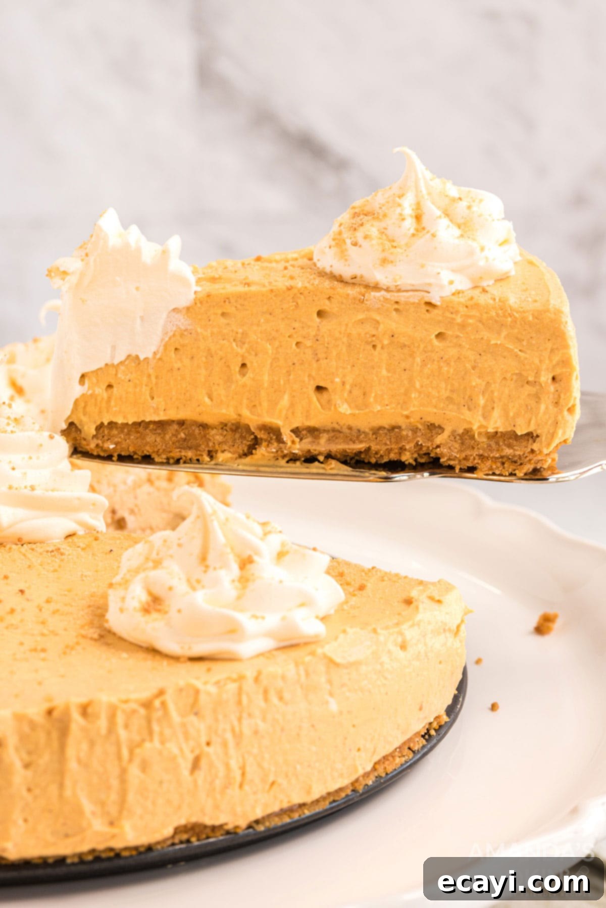 Serving a slice of No-Bake Pumpkin Cheesecake A slice of creamy no-bake pumpkin cheesecake being removed from the springform pan, showcasing its smooth texture and golden graham cracker crust.