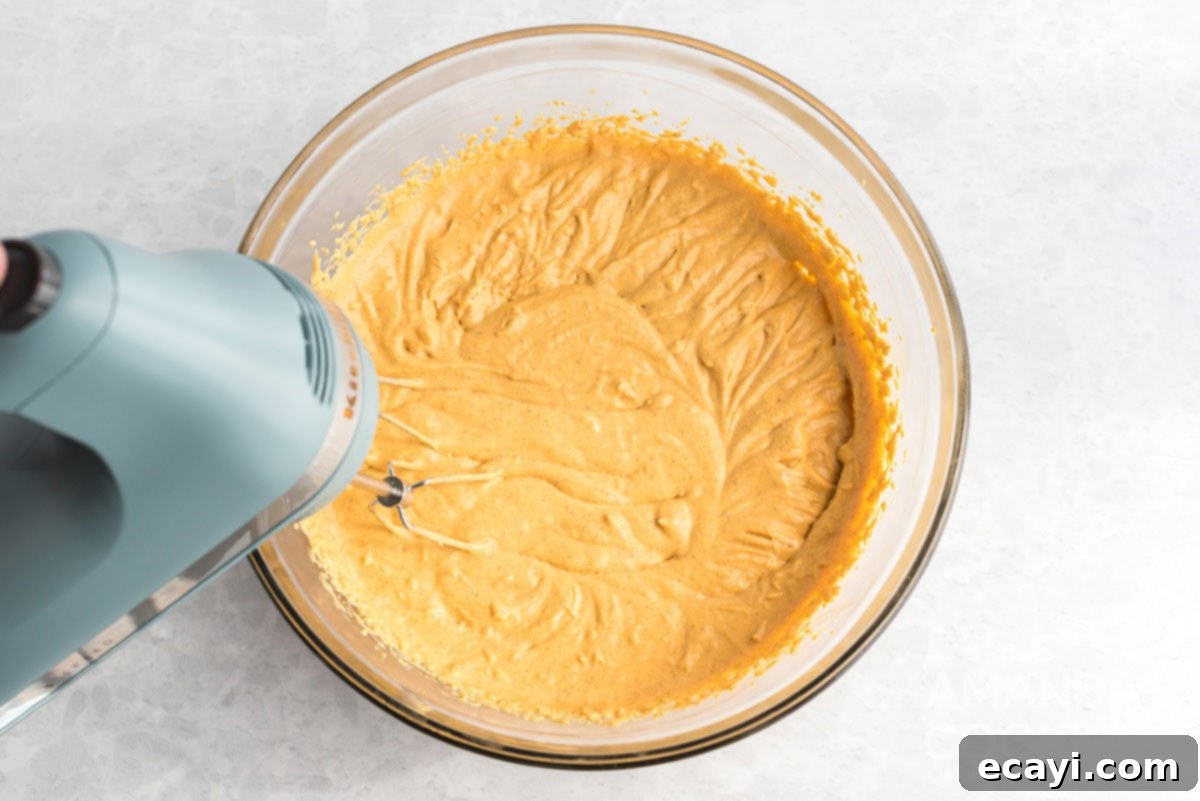 Dreamy No-Bake Pumpkin Perfection 7 An electric mixer actively blending cream cheese, pumpkin puree, sugar, and spices into a smooth, creamy pumpkin cheesecake batter.