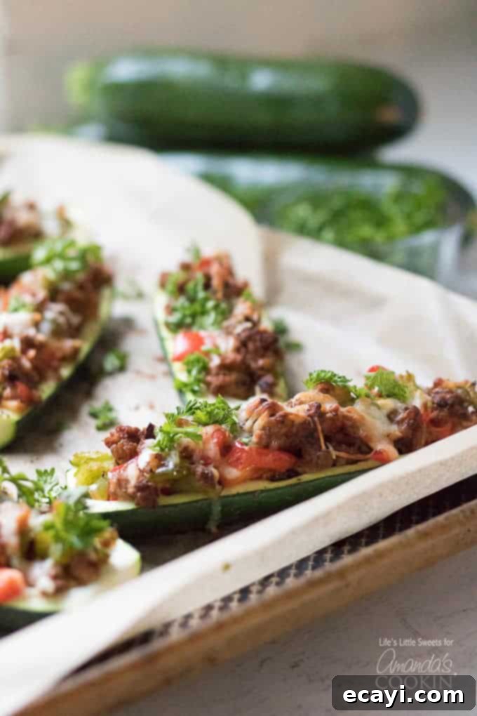 These colorful stuffed zucchini boats are a savory and delicious dinner packed with lean protein and a healthy serving of vegetables. Stuffing zucchini with lean ground turkey, fresh peppers, onions, and grated cheese makes for a tasty low-carb dinner and is a great way to use up all that garden zucchini! #zucchiniboats #stuffedzucchini #zucchinirecipes #lowcarbdinners #lowcarbrecipes #groundturkey #zucchini #amandascookin Two halves of stuffed zucchini boats on a serving platter