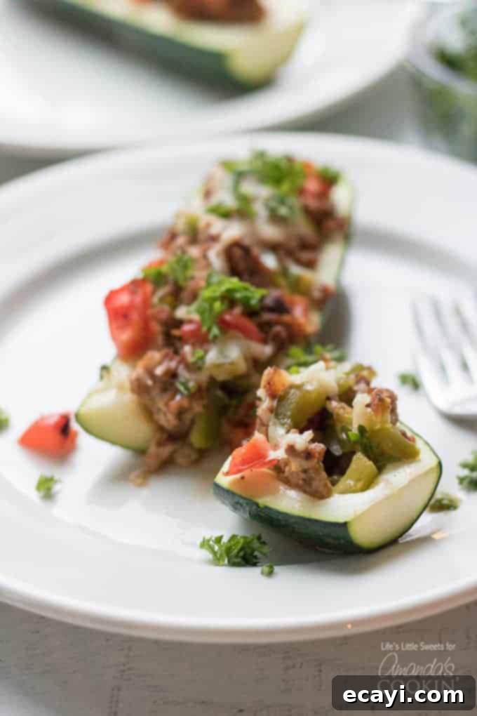 These colorful stuffed zucchini boats are a savory and delicious dinner packed with lean protein and a healthy serving of vegetables. Stuffing zucchini with lean ground turkey, fresh peppers, onions, and grated cheese makes for a tasty low-carb dinner and is a great way to use up all that garden zucchini! #zucchiniboats #stuffedzucchini #zucchinirecipes #lowcarbdinners #lowcarbrecipes #groundturkey #zucchini #amandascookin Close-up of a sliced stuffed zucchini boat showing the filling