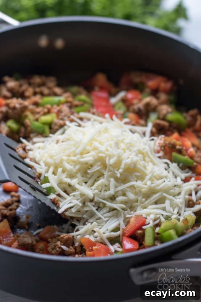 Zucchini Pockets 5 Shredded cheese being added to the cooked meat and vegetable mixture in a skillet