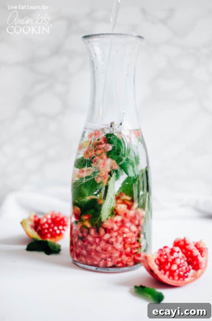 Holiday Detox Drink: Ingredients in Pitcher Ingredients for Holiday Detox Drink including fresh mint, pomegranate seeds, and honey, combined in a glass pitcher.