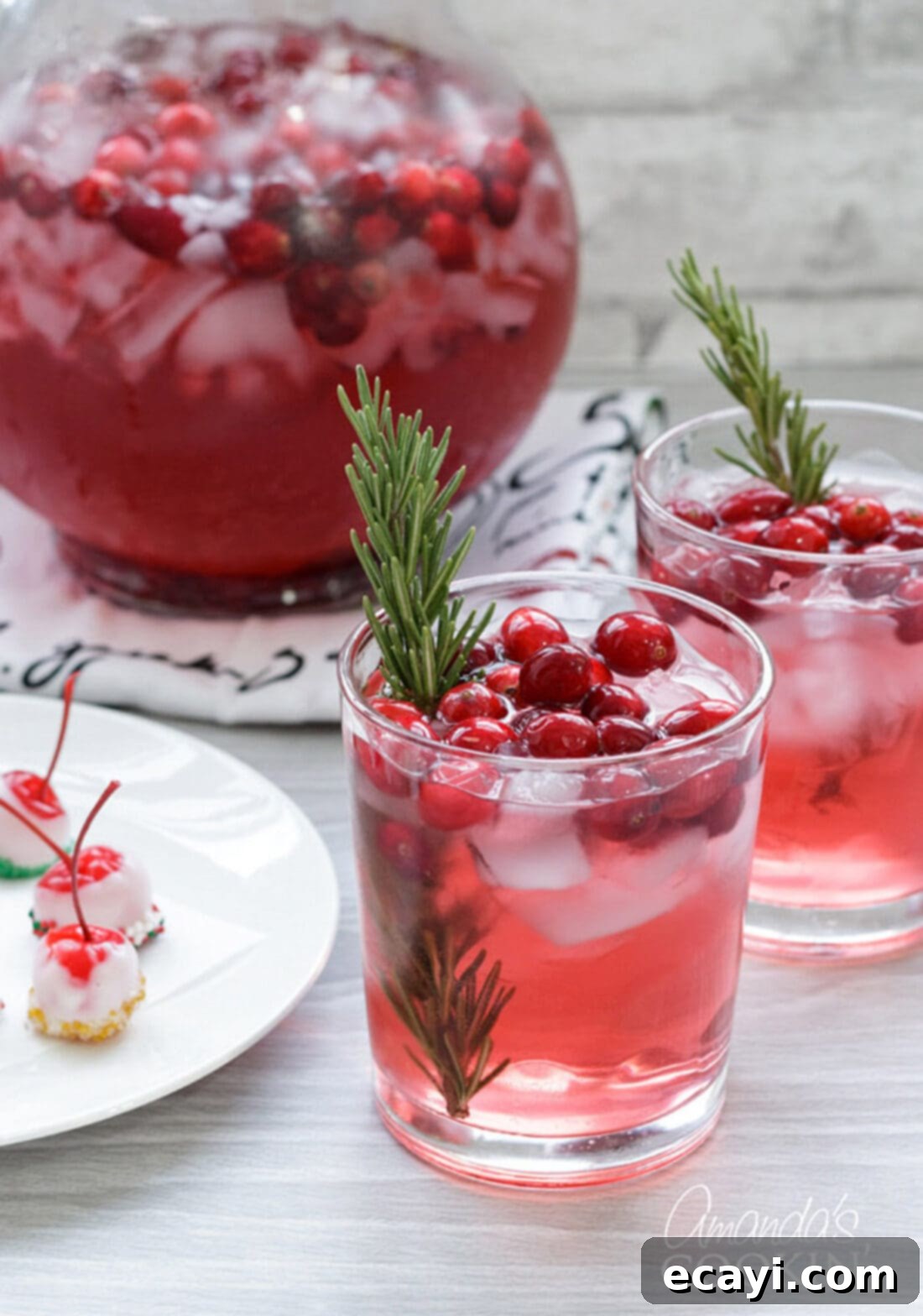 Cranberry Holiday Punch is perfect for your festive parties. Whip it up for your Thanksgiving gathering or a Christmas party! Two glasses and a pitcher of homemade Cranberry Holiday Punch garnished with rosemary, ready for festive gatherings.