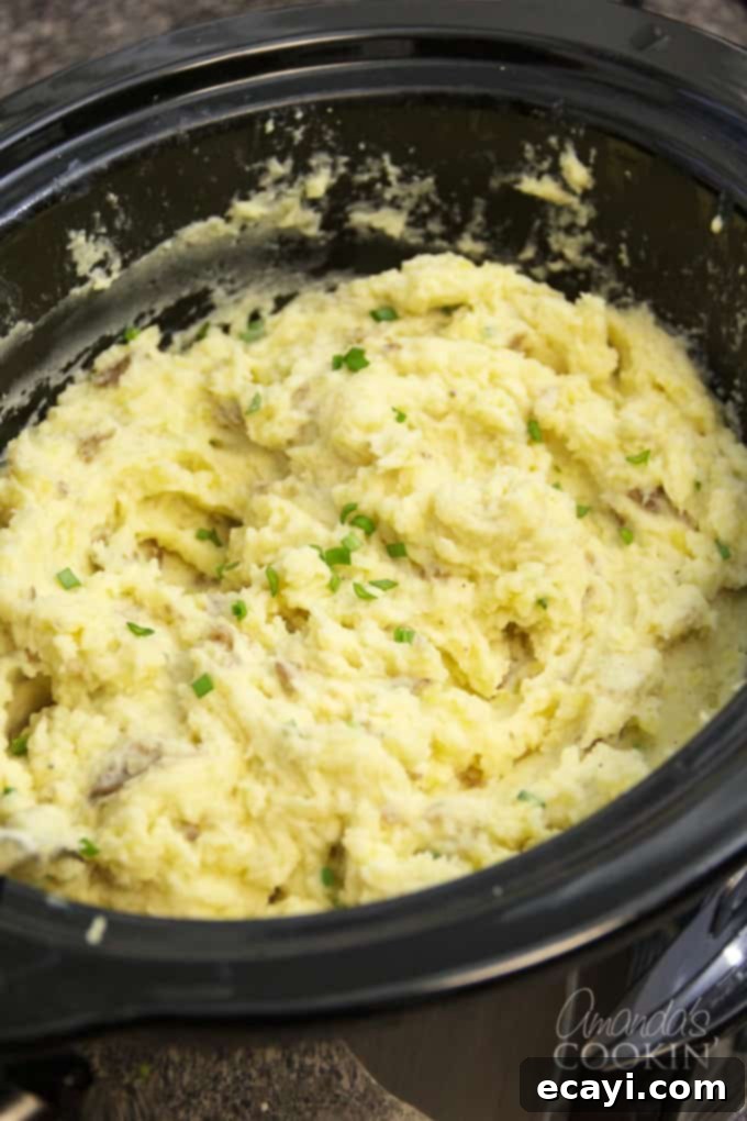 These Crockpot Mashed Potatoes are made with the skin on for extra flavor and nutrients, ideal for a stress-free holiday meal. #crockpotmashedpotatoes #slowcookermashedpotatoes #mashedpotatoes #thanksgivingrecipes #potatoes #chickenbroth #garlic #sourcream #creamcheese  Close-up of creamy Crockpot Mashed Potatoes, still in the slow cooker with a serving spoon, highlighting the rustic skin-on texture. Perfect for holiday dinners and busy weeknights.