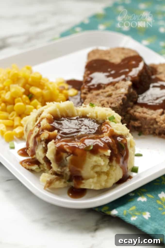Creamy Crockpot Mashed Potatoes, served with savory gravy, making a perfect side dish for any holiday gathering or family dinner. #crockpotmashedpotatoes #slowcookermashedpotatoes #mashedpotatoes #thanksgivingrecipes #potatoes #chickenbroth #garlic #sourcream #creamcheese  A plate featuring a generous serving of creamy mashed potatoes topped with rich brown gravy, ready for a delicious meal, evoking a sense of comfort and satisfaction.