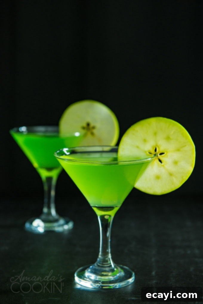 Classic Appletini Cocktails Two vibrant green Appletini martinis on a dark background, each garnished with a fresh apple wheel