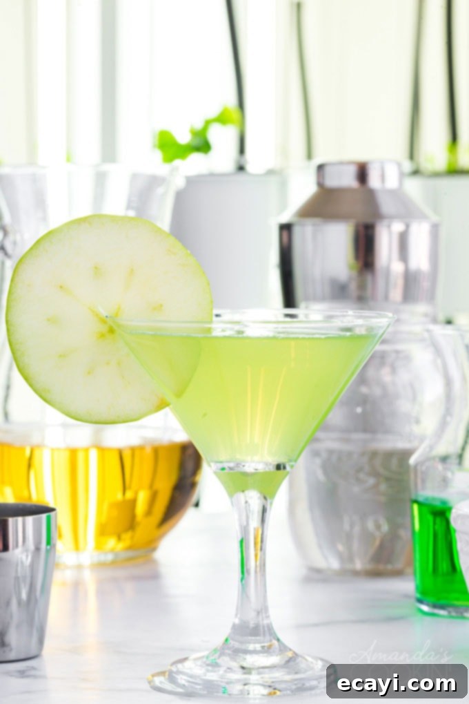 Refreshing Appletini in Martini Glass An Appletini cocktail served in a martini glass, with fresh apple slices and cocktail ingredients blurred in the background
