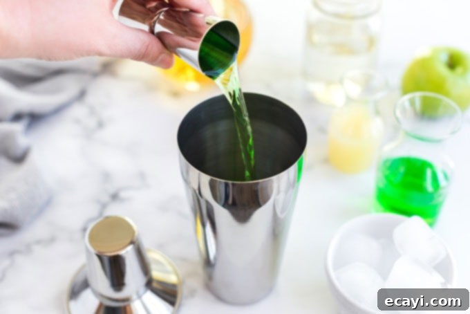Crisp Apple Charm 3 Pouring green apple vodka into a stainless steel cocktail shaker filled with ice