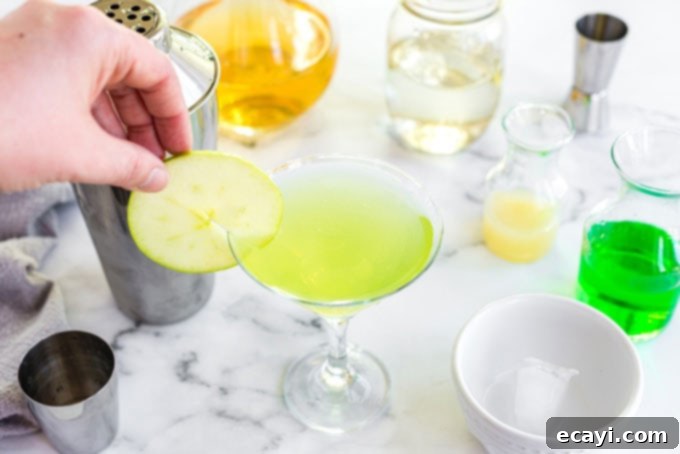 Crisp Apple Charm 7 Placing a thin, vibrant green apple wheel slice on the rim of a martini glass filled with an Appletini