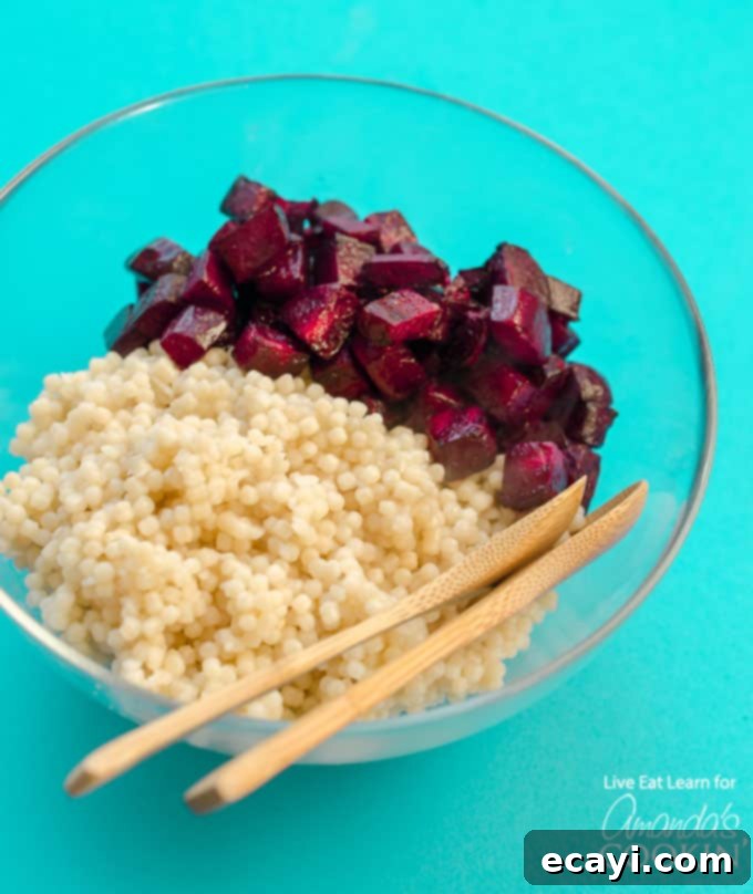 The beautiful fusion of pearl couscous and roasted beets creates a vibrant and delicious base for this easy Feta & Beet Salad. #couscous #feta #beets #dinnersides #sidedish #healthy #healthysides #salad #sidesalad #vegetarian Cooked pearl couscous mixed with diced roasted beets in a bowl, showcasing the beautiful pink color that makes this salad so appealing.