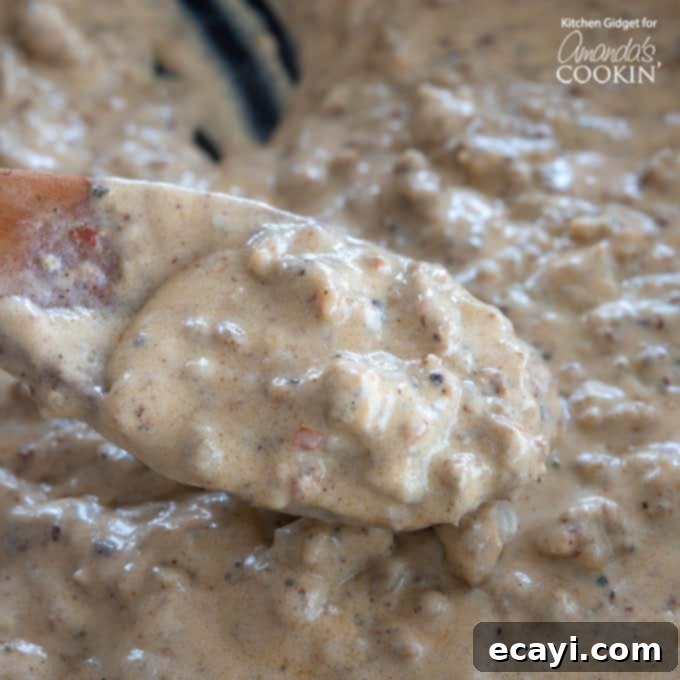 Hearty Country Gravy 3 Close-up view of thick, creamy sausage gravy simmering in a cast iron pan with a wooden spoon
