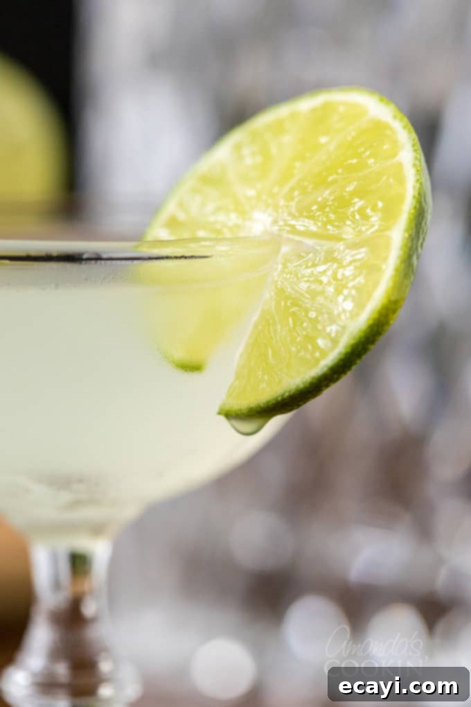 Learn to make a classic Gimlet cocktail in your own kitchen. Be sure to pull out the coupe glasses for a traditional lime adult drink you will love. #gimletrecipe #gimlet #gimletcocktail #cocktails #cocktailrecipes #gin #limejuice #ginrecipes #gindrinks #classiccocktails close up of gimlet cocktail in coupe glass with lime wheel garnish