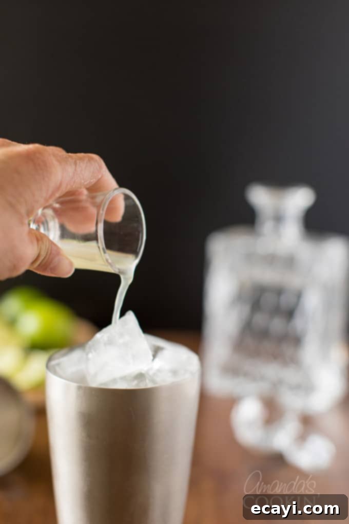 Learn to make a classic Gimlet cocktail in your own kitchen. Be sure to pull out the coupe glasses for a traditional lime adult drink you will love. #gimletrecipe #gimlet #gimletcocktail #cocktails #cocktailrecipes #gin #limejuice #ginrecipes #gindrinks #classiccocktails pouring lime juice into cocktail shaker