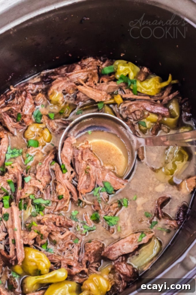 This Mississippi pot roast is slowly cooked in the crockpot until it's fall-apart tender then served with a rich gravy made w/ ranch & pepperoncini peppers. Close-up of Mississippi pot roast simmering in a crockpot, with vibrant green pepperoncini peppers visible.