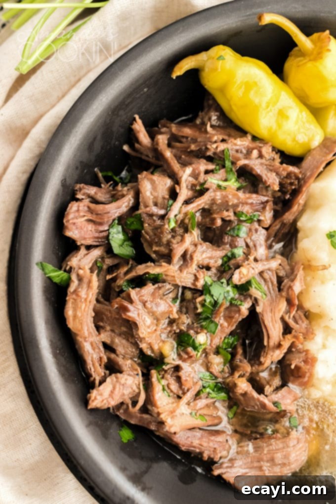 This Mississippi pot roast is slowly cooked in the crockpot until it's fall-apart tender then served with a rich gravy made w/ ranch & pepperoncini peppers. Close-up of extremely tender, stringy Mississippi pot roast being lifted by a fork from a bowl, highlighting its fall-apart texture.