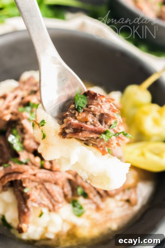 This Mississippi pot roast is slowly cooked in the crockpot until it's fall-apart tender then served with a rich gravy made w/ ranch & pepperoncini peppers. A fork pulling apart a piece of tender Mississippi pot roast, illustrating its incredibly soft and succulent texture.