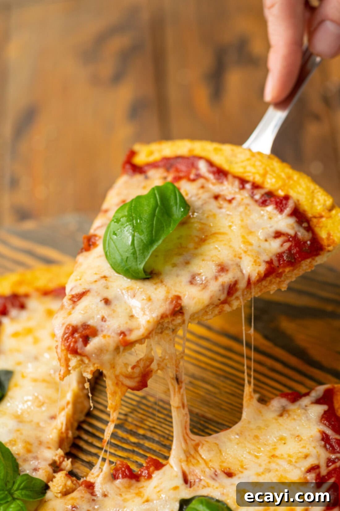 Cauliflower Power Crust 3 A delectable slice of cauliflower pizza crust being lifted, topped with vibrant basil leaves and melted cheese, highlighting its sturdy build and mouth-watering appeal.