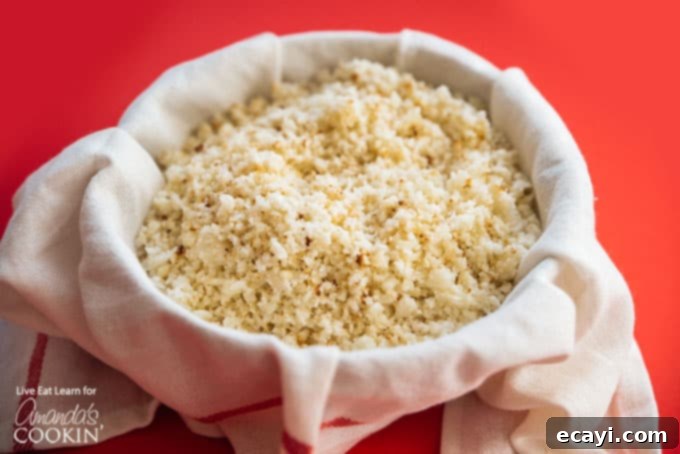 Cauliflower Power Crust 4 Grated cauliflower in a cheesecloth, being squeezed to remove excess moisture, demonstrating the crucial step for a crispy crust.