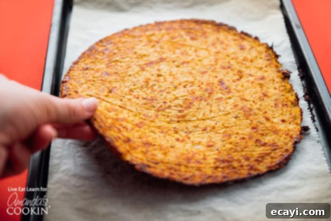Cauliflower Power Crust 5 A golden-brown cauliflower pizza crust being carefully lifted off a baking sheet, showcasing its perfectly baked and sturdy texture.