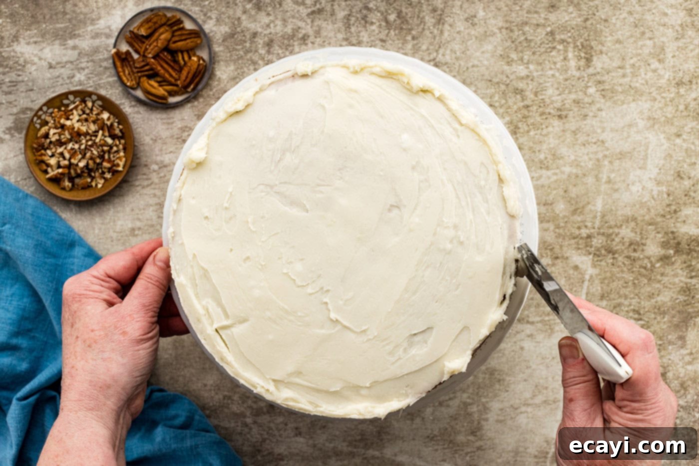 Spiced Carrot Delight 11 A bench scraper deftly removing excess cream cheese frosting from the side of a carrot cake on a turntable, creating a trendy 'naked cake' effect.