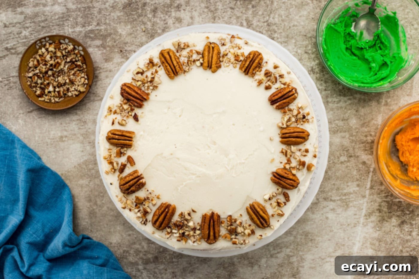 Spiced Carrot Delight 12 Twelve pecan halves arranged neatly around the edge of a carrot cake, with a scattering of chopped pecans across the top, ready for further decoration.