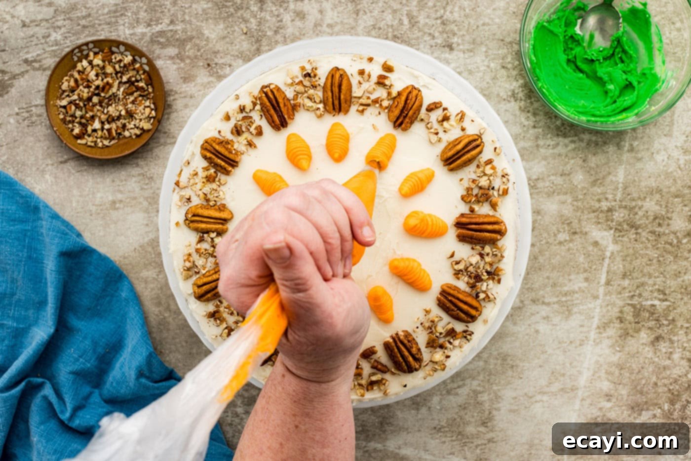 Spiced Carrot Delight 13 A hand expertly piping small, orange carrot shapes onto the top of a frosted carrot cake using a piping bag and a Wilton tip.