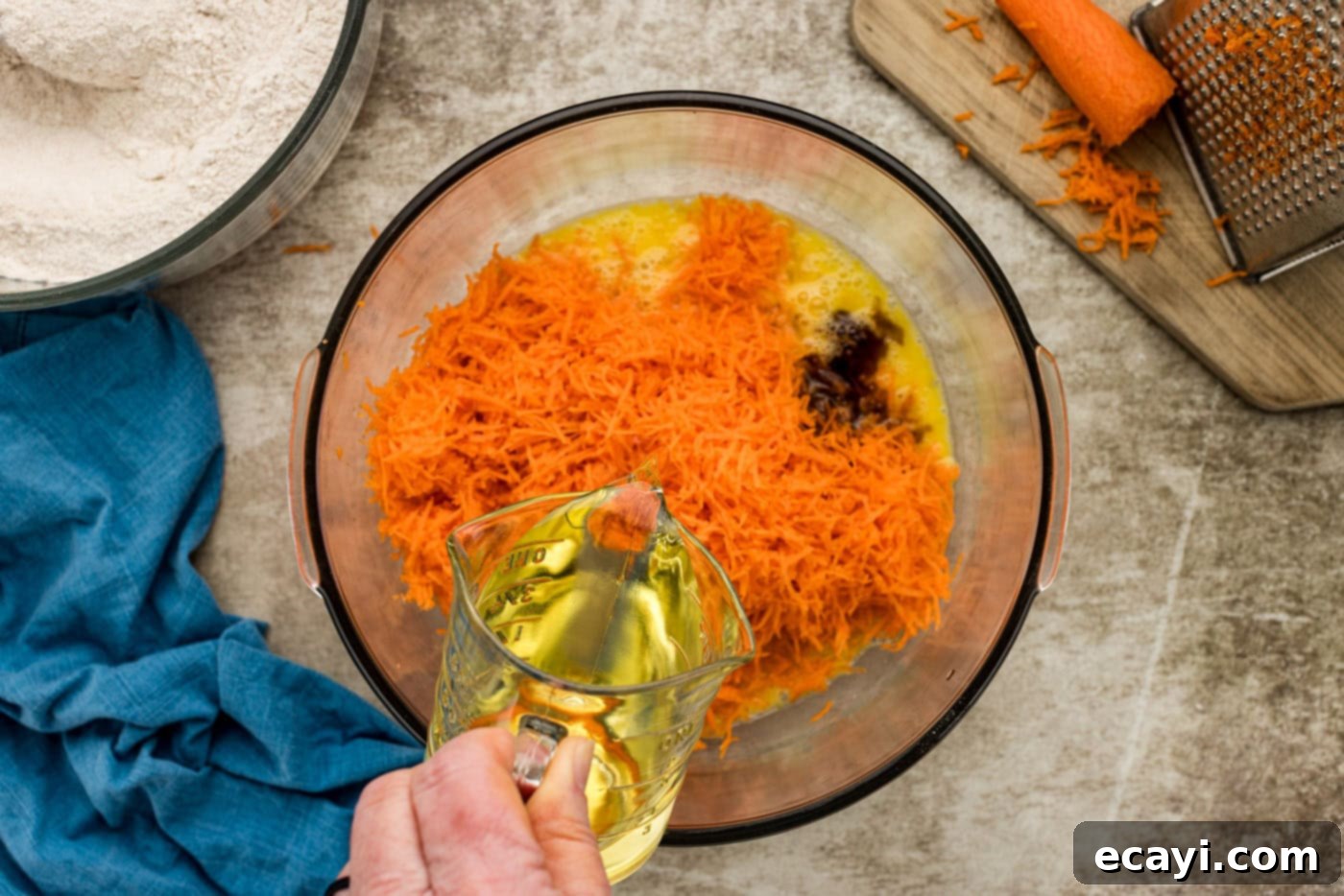 Spiced Carrot Delight 6 Canola oil being poured into a bowl containing finely shredded carrots, beaten eggs, and vanilla extract, ready to be combined.