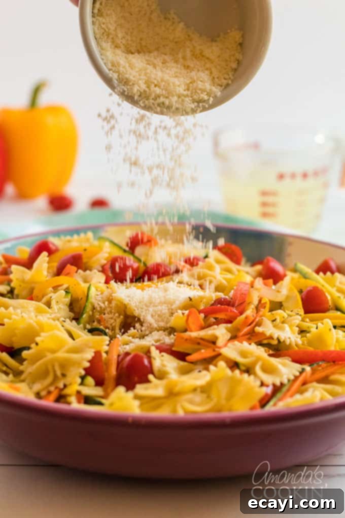 Pasta Primavera is a simple dish, ideal for weeknights, full of fresh vegetables and light on the sauce. A family friendly meal you'll love. #pastaprimavera #pastarecipes #vegetarian #zucchini #bellpeppers #dinner #dinnerrecipes #meatlessmondays parmesan cheese being sprinkled over pasta primavera