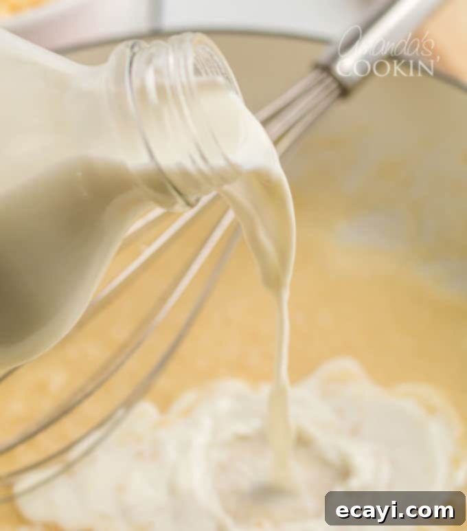 Achieve ultimate creaminess! Gradually whisk milk into your roux for the perfect Panera mac and cheese sauce base. #panera #macandcheese #macaroni #cheese #copycatrecipes #dinnersides A bottle of milk being slowly poured into a saucepan, as it's whisked into the butter and flour roux to form the béchamel sauce.