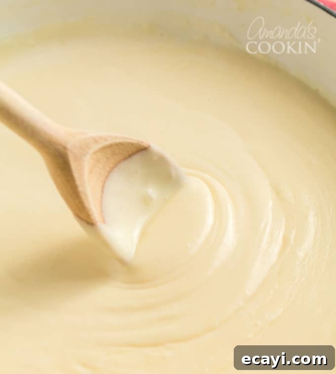 Stirring the rich cheese sauce to perfection, ensuring every ingredient is blended for the ultimate creamy Panera mac and cheese. #panera #macandcheese #macaroni #cheese #copycatrecipes #dinnersides A wooden spoon actively stirring a luxurious, golden cheese sauce to ensure it reaches a perfect, smooth, and lump-free consistency.