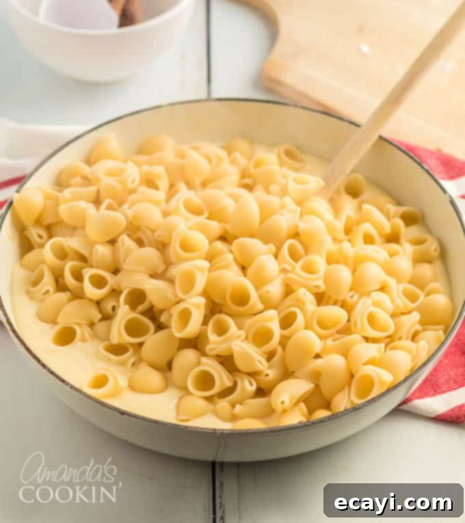 The final flourish: combining the cooked pasta with the silky cheese sauce for a truly authentic and delicious Panera mac and cheese experience. #panera #macandcheese #macaroni #cheese #copycatrecipes #dinnersides A close-up view of creamy cheese sauce being mixed into a bowl of perfectly cooked pasta, transforming it into homemade Panera mac and cheese.