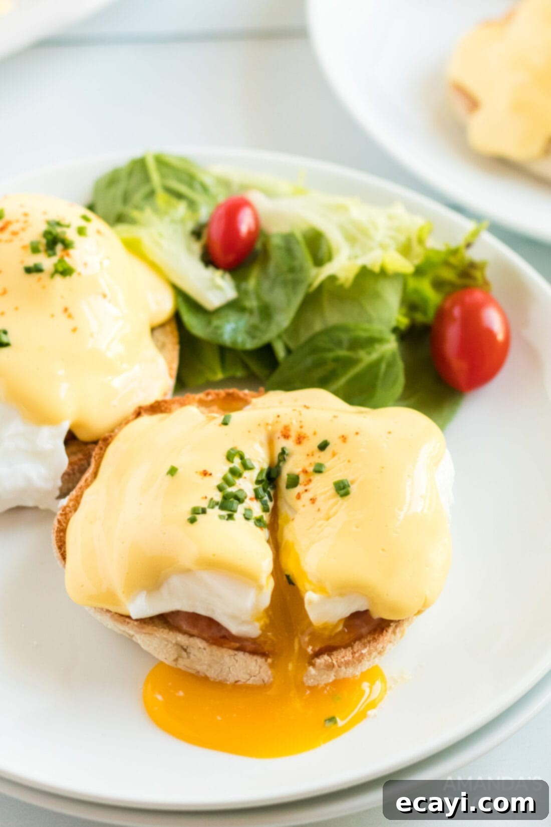 Eggs Benedict is a delicious open-faced English muffin sandwich. Topped with a perfectly poached egg, Canadian bacon, and a rich, creamy hollandaise sauce. #eggsbenedict #breakfast #breakfastrecipes #mothersdayrecipes #brunch #sandwich #breakfastsandwich #hollandaise cut open eggs benedict on a plate