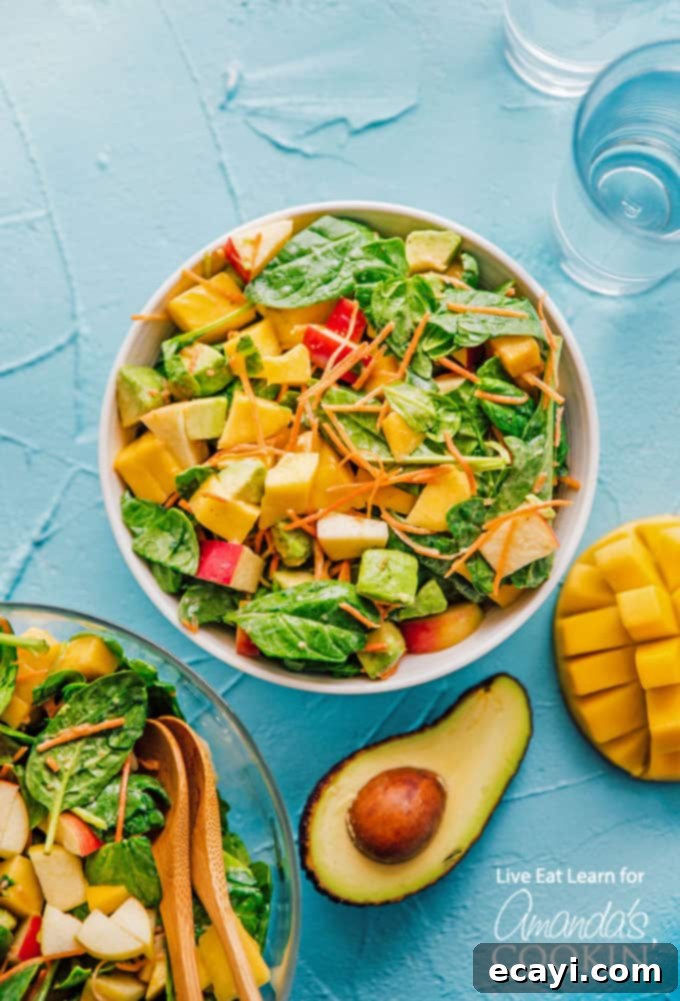 This delicious spinach salad is packed with protein-rich leafy spinach, sweet mango, and healthy fats from avocado. Perfect for summer! #spinachsalad #avocadosalad #mangosalad #summersalad #leafygreens #freshsaladrecipes #spinachsaladrecipes #meatlesssalad #amandascookin Spinach salad overhead shot with avocado, mango and apple, showcasing its fresh ingredients and vibrant colors