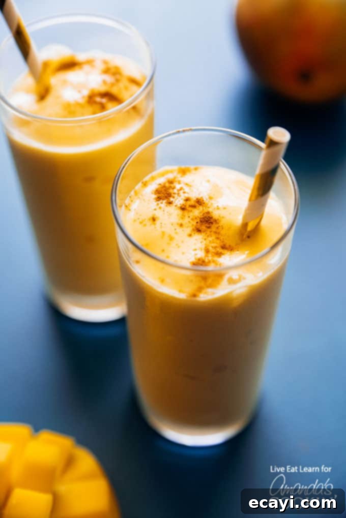 An authentic mango lassi is a delicious yogurt and mango smoothie using traditional Indian spices. This homemade mango lassi smoothie is a sweet treat that's totally delicious and easy to make. #mangolassi #mangolassismoothie #smoothierecipes #sweetsmoothies #mangosmoothie #amandascookin A vibrant yellow mango lassi smoothie, garnished with a sprinkle of cinnamon, photographed from above with a rustic background.