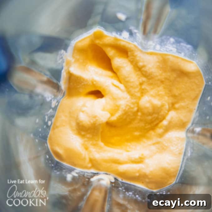 A mango lassi is a delicious yogurt and mango smoothie using Indian spices. This mango lassi smoothie is a sweet treat that's totally delicious. #mangolassi #mangolassismoothie #smoothierecipes #sweetsmoothies #mangosmoothie #amandascookin The blended ingredients for mango lassi, showcasing a smooth, uniform texture in a blender jug.