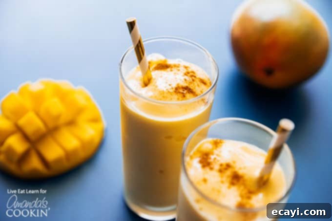 A mango lassi is a delicious yogurt and mango smoothie using Indian spices. This mango lassi smoothie is a sweet treat that's totally delicious. #mangolassi #mangolassismoothie #smoothierecipes #sweetsmoothies #mangosmoothie #amandascookin Two glasses of mango lassi smoothies, each with a straw, arranged invitingly on a table.