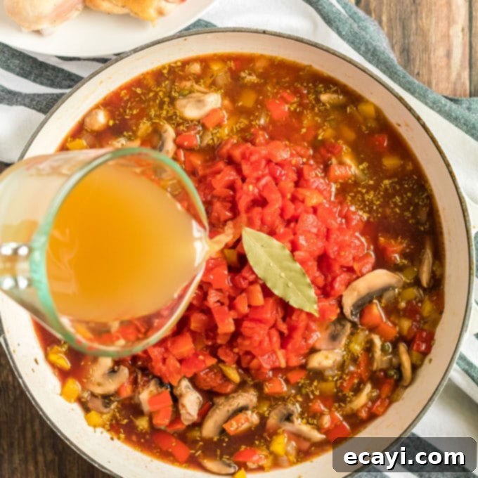 Combining diced tomatoes, chicken broth, and a bay leaf with sautéed vegetables and wine for the Stovetop Chicken Cacciatore sauce. #tomatoes #chickenbroth #bayleaf #stewbase tomatoes, broth, and bay leaf over ingredients in skillet