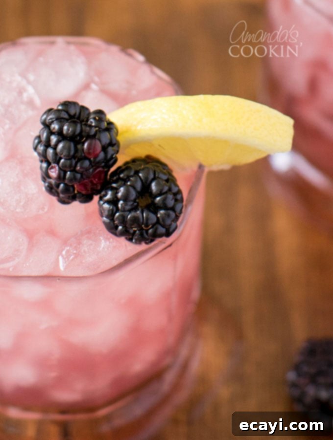 Bramble Cocktail: A Refreshing Gin and Blackberry Drink for Summer Close-up shot of a Bramble cocktail, showcasing the vibrant blackberry liqueur drizzled over ice with lemon and fresh blackberries as garnish.