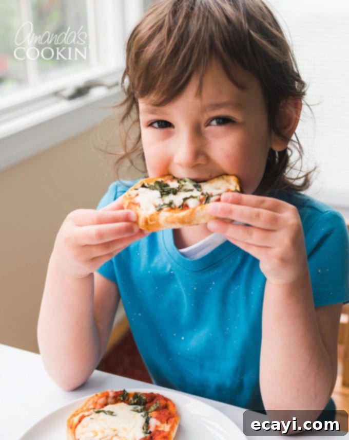Muffin Pizza Creation Bar 11 A happy little girl taking a joyous bite from an English muffin pizza, her face expressing pure enjoyment of her homemade snack