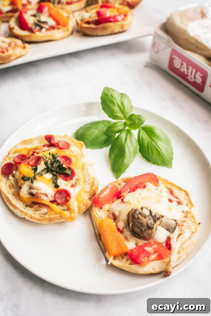 Muffin Pizza Creation Bar 3 Two perfectly baked English muffin pizzas topped with melted cheese and pepperoni, presented on a white plate