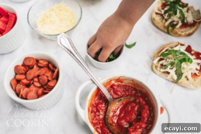 Muffin Pizza Creation Bar 8 A small child's hand gently taking fresh basil leaves from a bowl of herbs, ready to add to their English muffin pizza