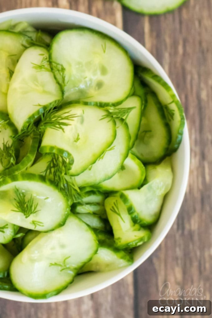 This classic cucumber salad is made with a homemade vinegar dressing and fresh dill. It's the vinegar cucumber salad your grandma used to make! #cucumbersalad #vinegarcucumbersalad #potluckrecipes #saladrecipes #cucumbersaladrecipes #amandascookin Close-up view of thinly sliced cucumbers in a bowl, coated in dressing, ready for chilling