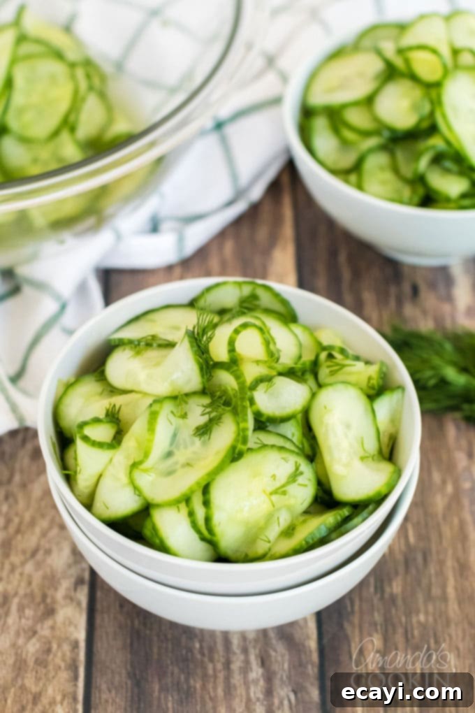 This classic cucumber salad is made with a homemade vinegar dressing and fresh dill. It's the vinegar cucumber salad your grandma used to make! #cucumbersalad #vinegarcucumbersalad #potluckrecipes #saladrecipes #cucumbersaladrecipes #amandascookin Freshly prepared cucumber salad in a serving bowl, garnished with a sprig of fresh dill, ready to be enjoyed