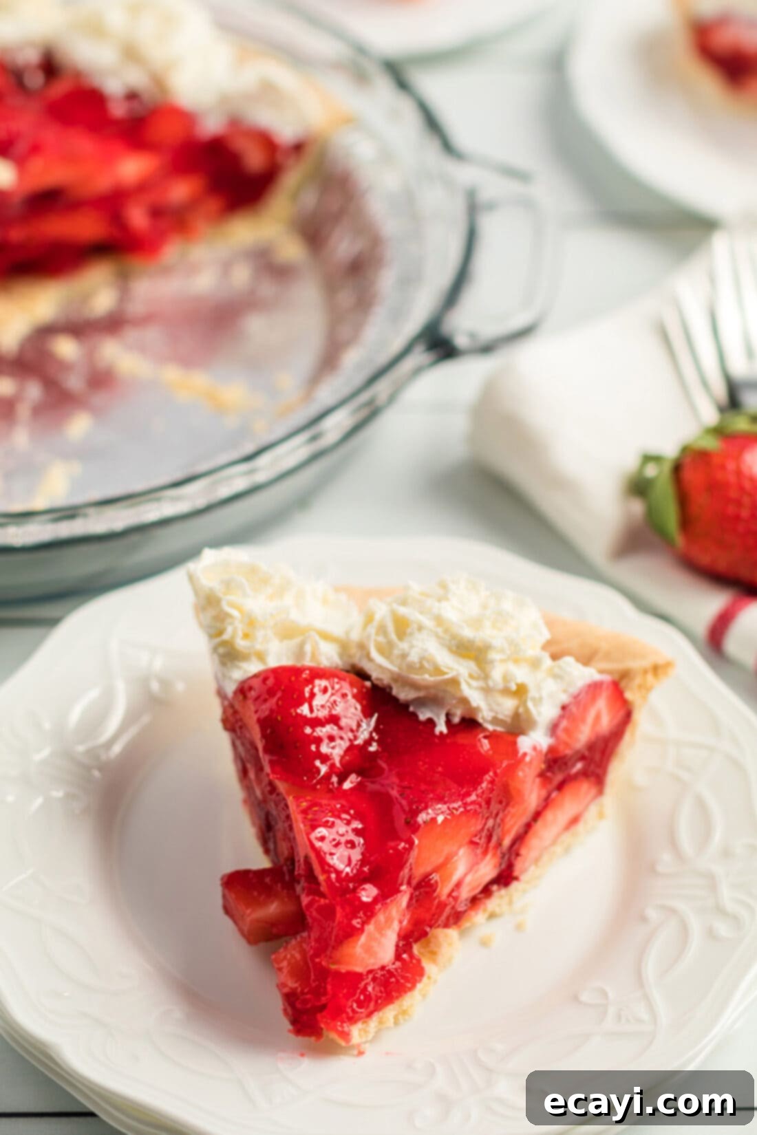 A delicious single slice of Jello Strawberry Pie on a plate. A single, perfectly portioned slice of Jello Strawberry Pie resting on a white plate, showcasing layers of fresh strawberries and a glossy, set gelatin filling, topped with a dollop of whipped cream.