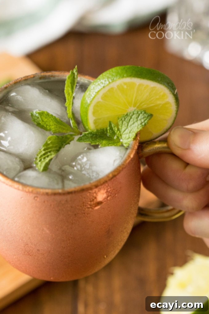 How do you make a Moscow Mule? Vodka, spicy ginger beer, and lime juice come together to make the best Moscow Mule cocktail! And of course, don't forget the mint! #moscowmule #moscowmulerecipe #howtomakeamoscowmule #cocktailrecipes #vodkarecipes #amandascookin hand holding a copper mug of moscow mule
